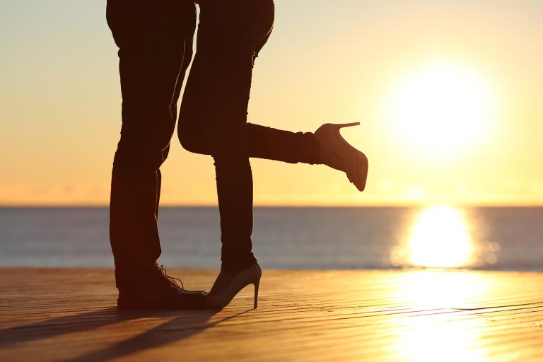 Silhouette of a couple's legs while embracing on the beach at sunset